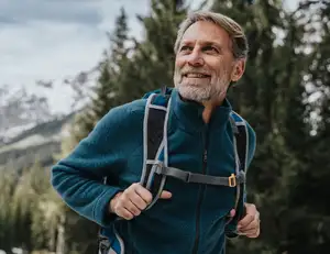 Älterer Mann mit Rucksack beim Wandern im Wald.