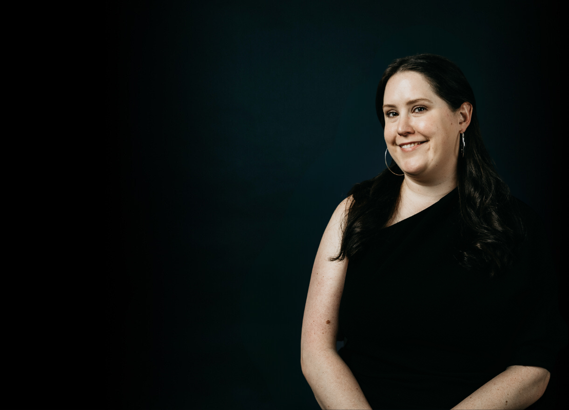 Picture of Luminary employee, Claire standing in front of a black screen in a green top