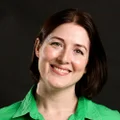 Picture of Luminary employee, Anna Potter smiling standing in front of a black screen in a green top
