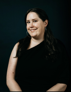 Picture of Luminary employee, Claire smiling standing in front of a black screen in a black top