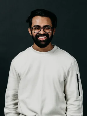Picture of Luminary employee, Adi smiling at the camera with a black background.