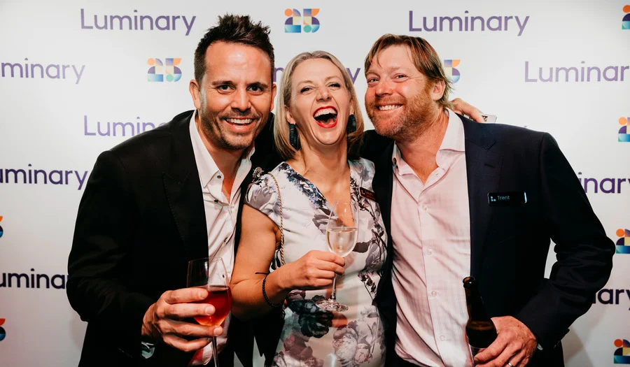 Two men and a woman smiling with glasses of champagne at a party 