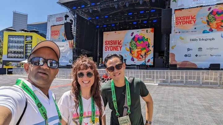 Group picture of Emm, Grace and Kelvin standing in front of a stage at SXSW 2023 