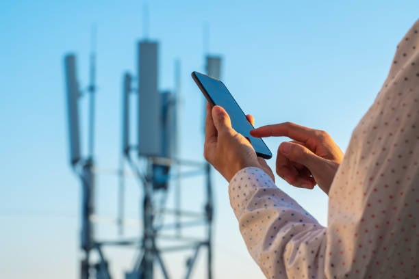 man using phone in front of a phone mast