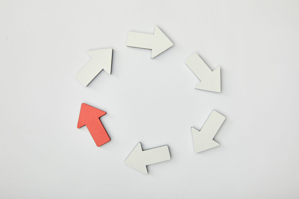 Top view of white arrows and one red arrow pointing at each other to form a circle.