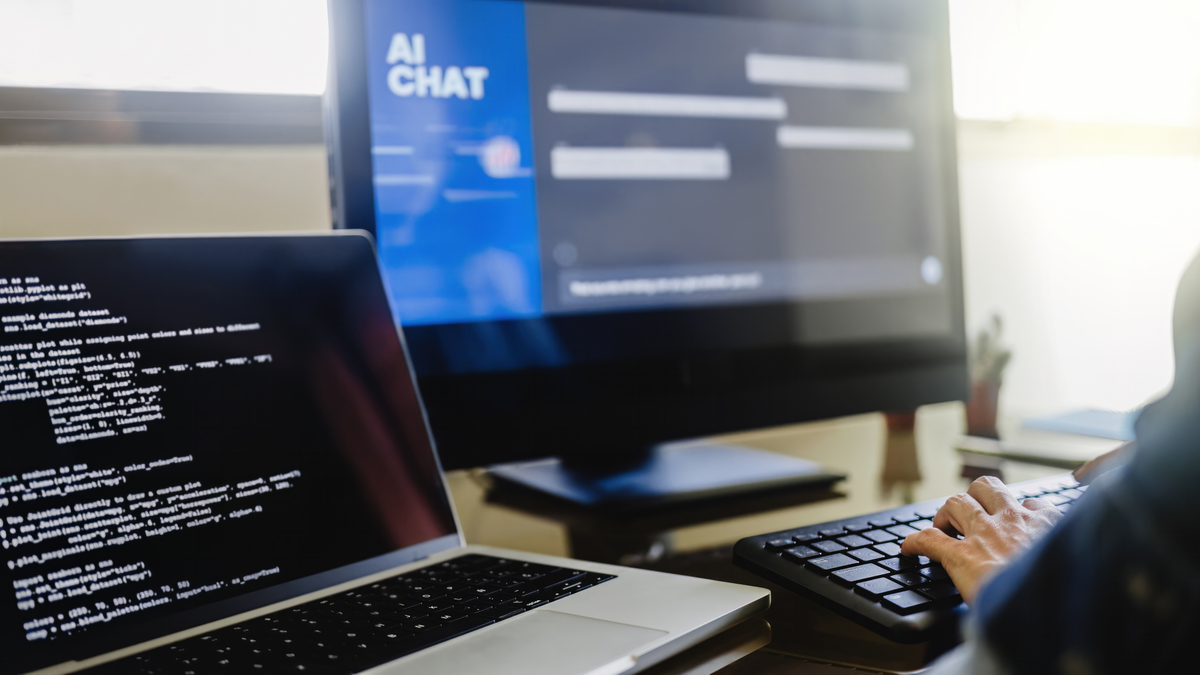 Person typing on screen with AI chat and laptop on side with screen of code.