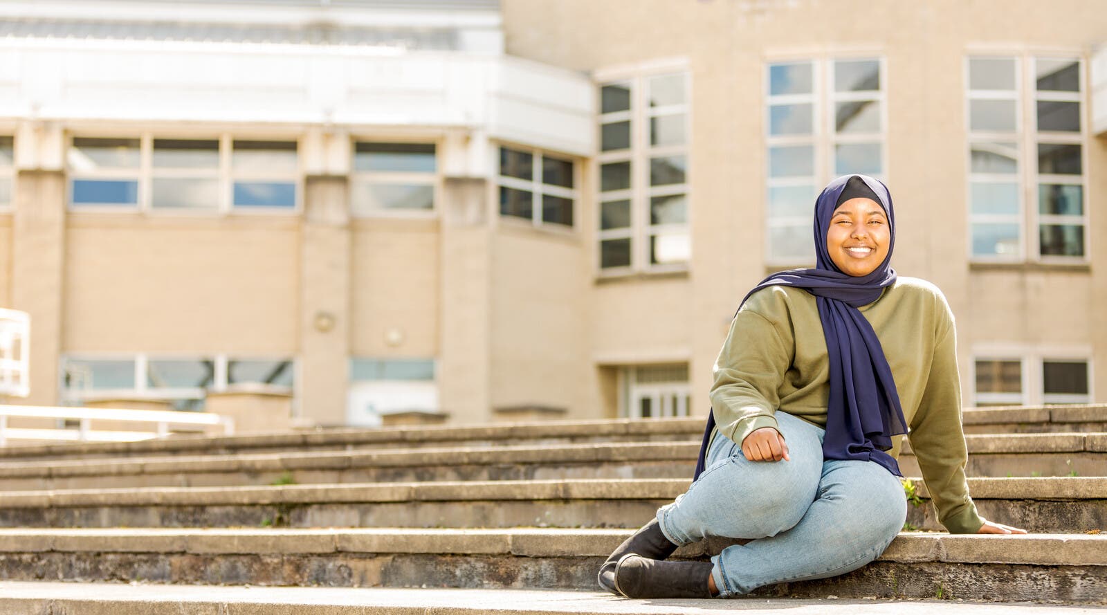 Student smiling and sitting on steps outside campus