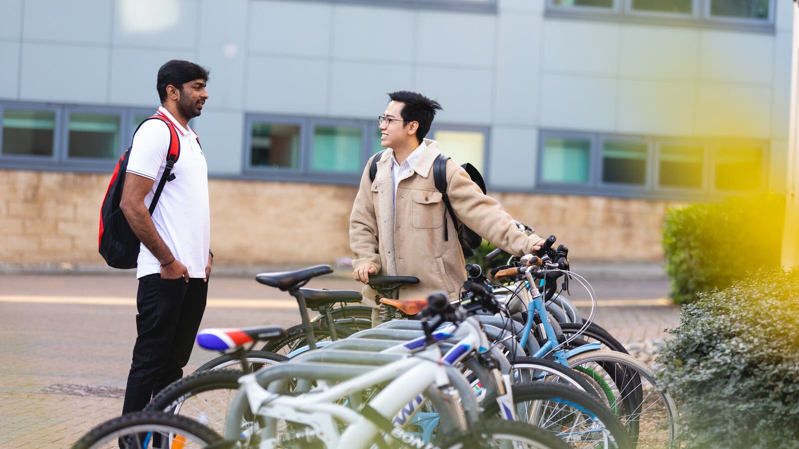 Two students talking outside campus by bike racks