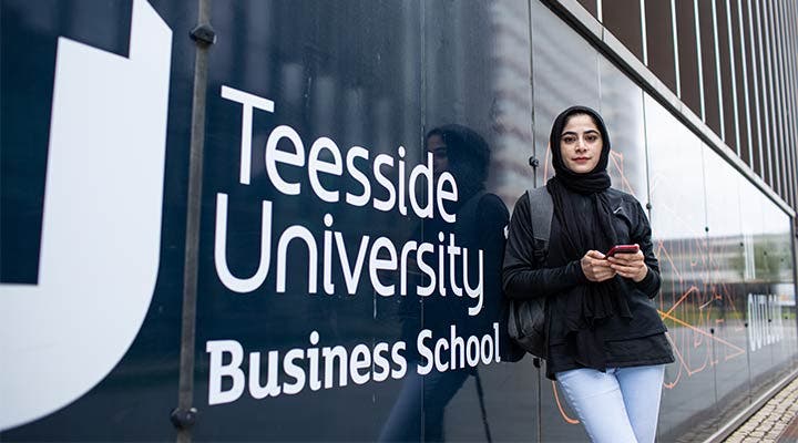 Student leaning on Teesside University Business School sign