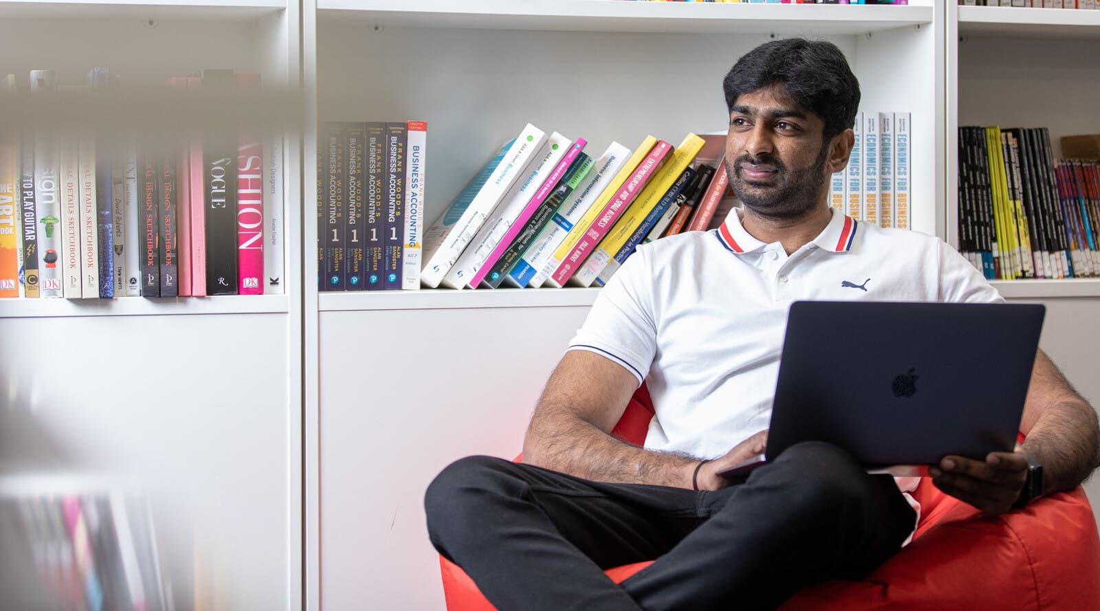 An Indian student using a laptop in front of books.