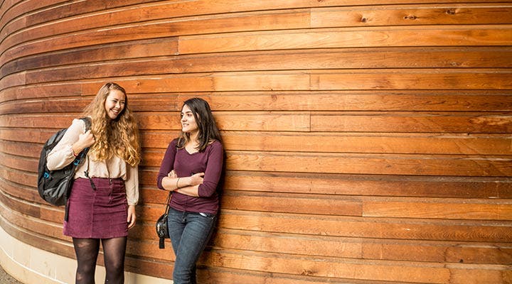Students talking and leaning against a wall