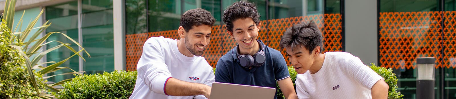 Three students on a bench looking at a laptop