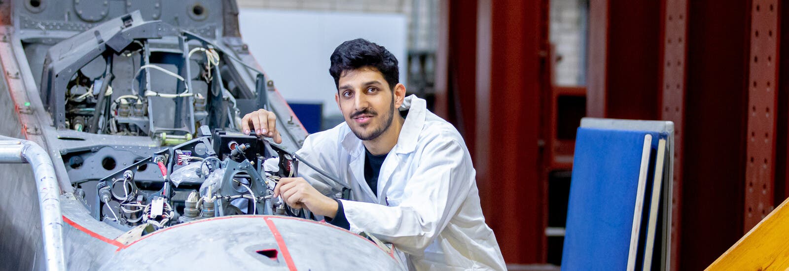 Engineering student in a lab coat working on an engine.