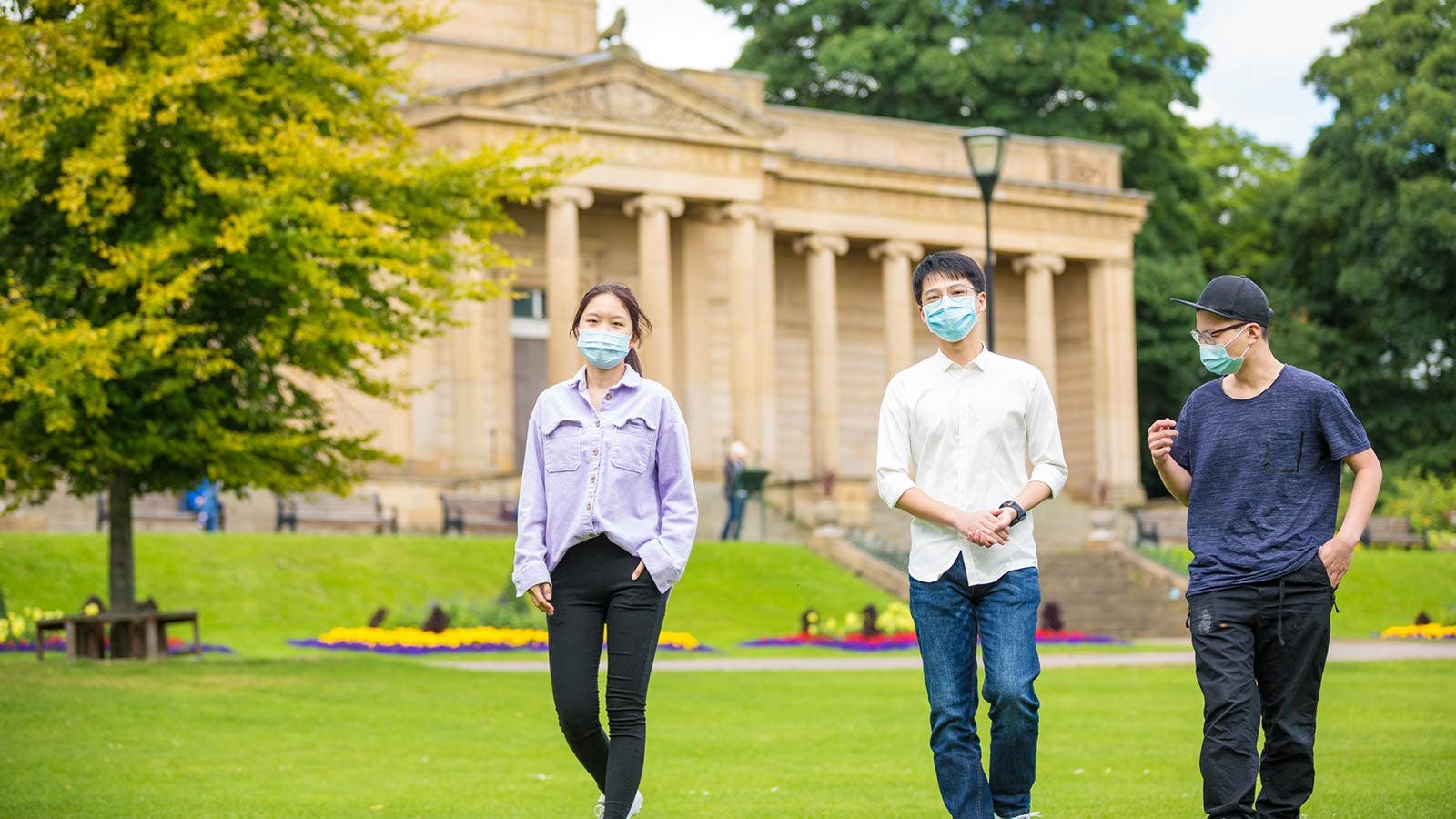 Students wearing face coverings walking across campus lawn
