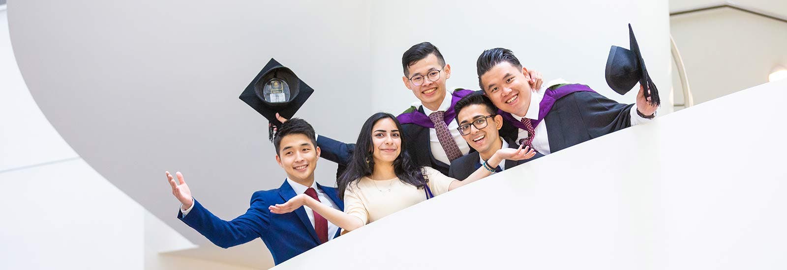 Graduates smiling on staircase holding mortar boards