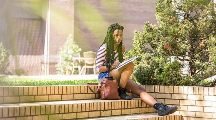 Student writing and sitting on stone steps outside campus