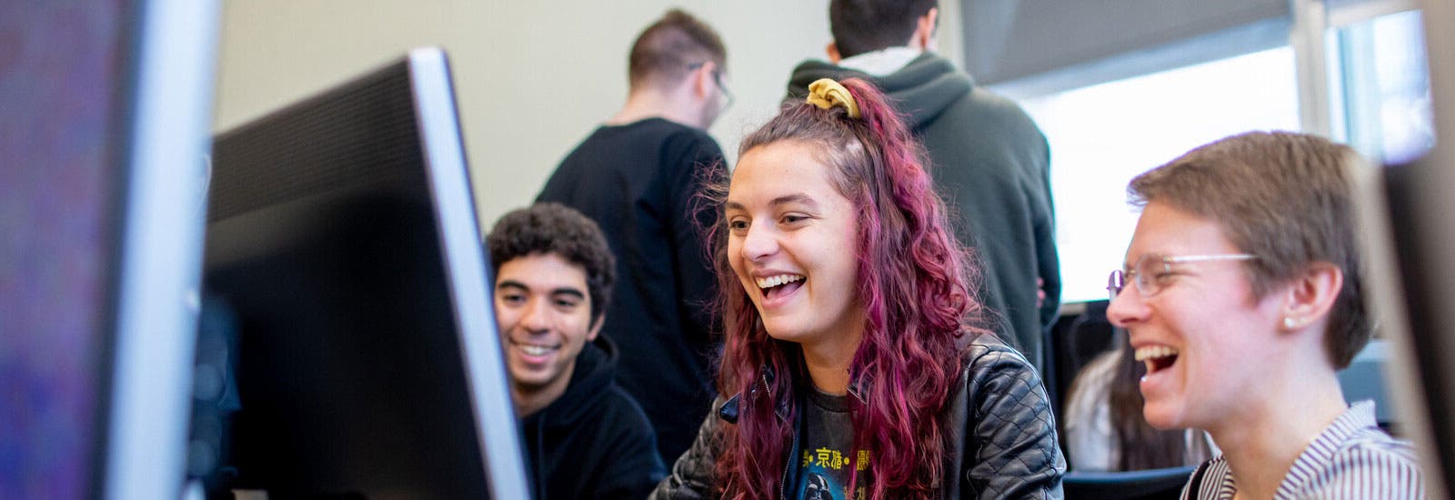 Three students laughing and using a computer