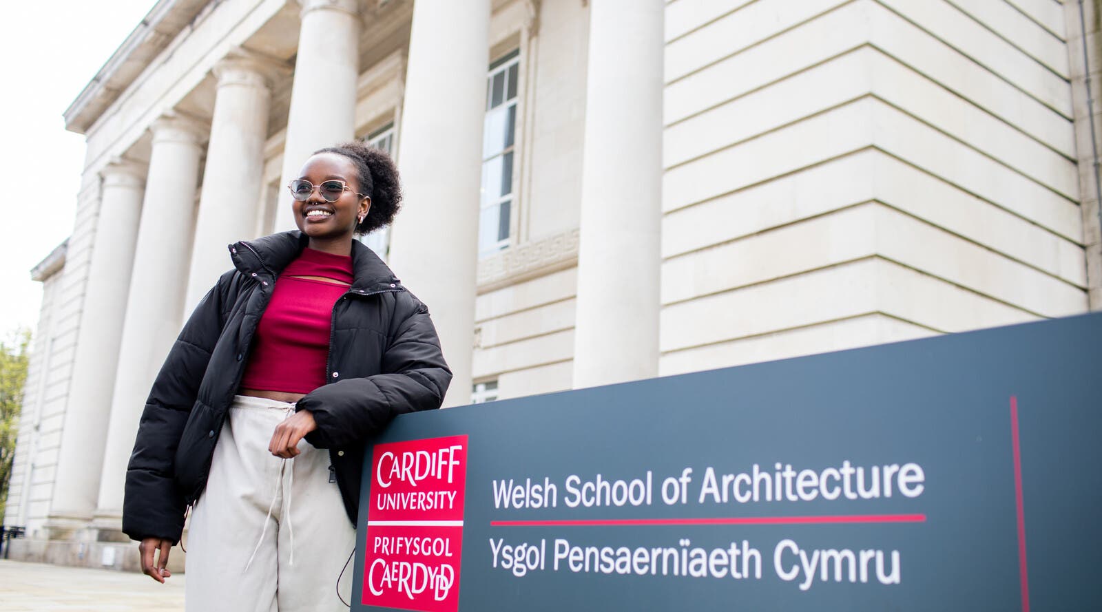 Student smiling and leaning on Cardiff architecture sign