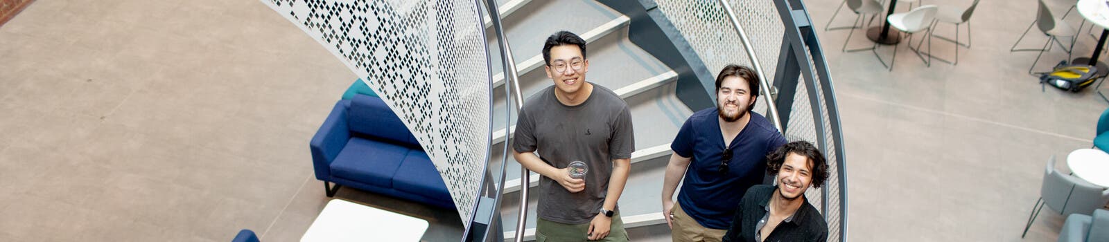 Three students standing on stairs on campus, smiling
