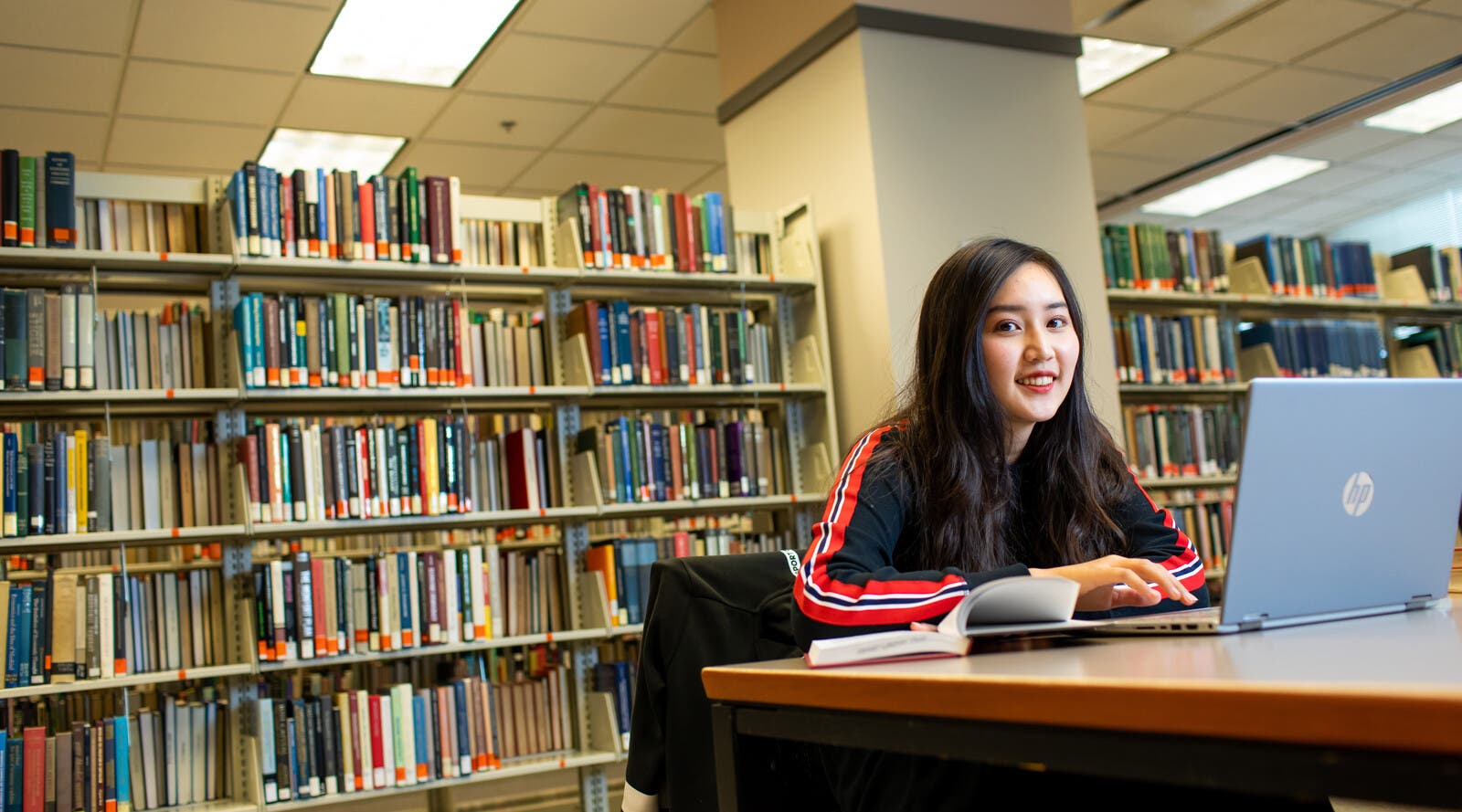 Student smiling and using laptop in library