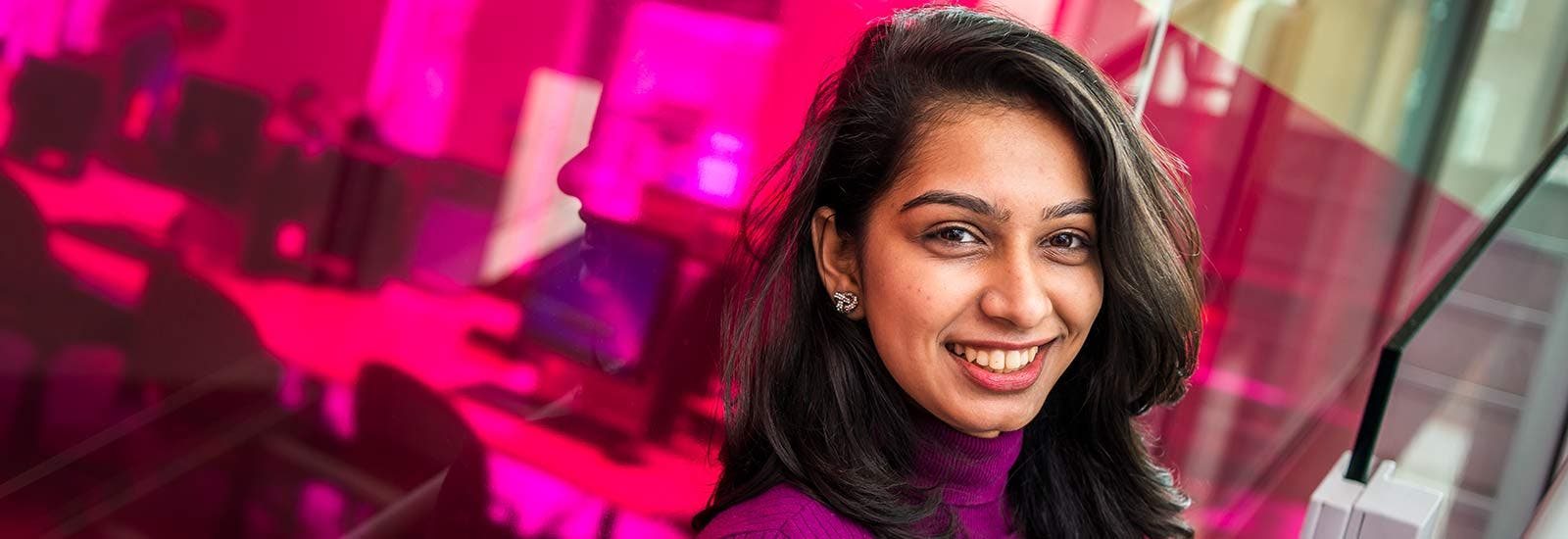 Student smiling in front of pink backdrop