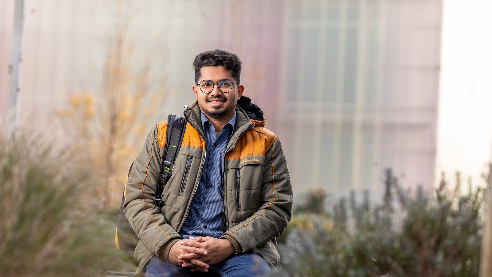 Student smiling and sitting on a wall outside campus