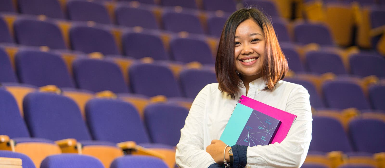 Student smiling in lecture hall and holding textbooks