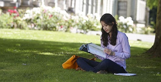 Student reading book on grass outside campus