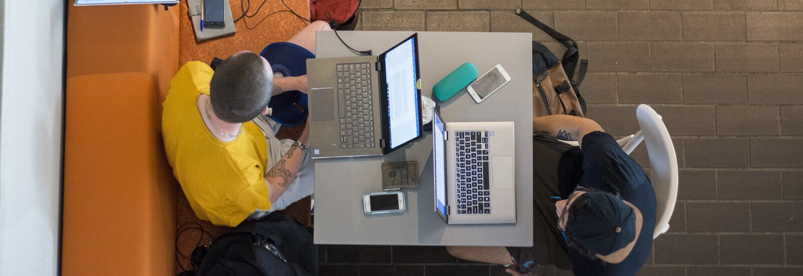 Two students studying remotely on laptops in a cafe