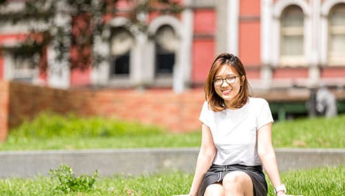 Student sitting on grass and smiling outside campus