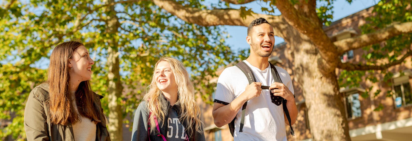 Three students smiling and walking in the sunshine.