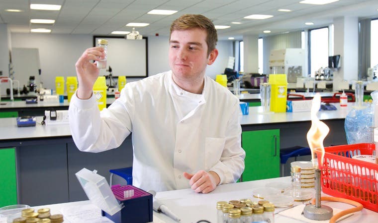 Science student holding up vial in lab coat