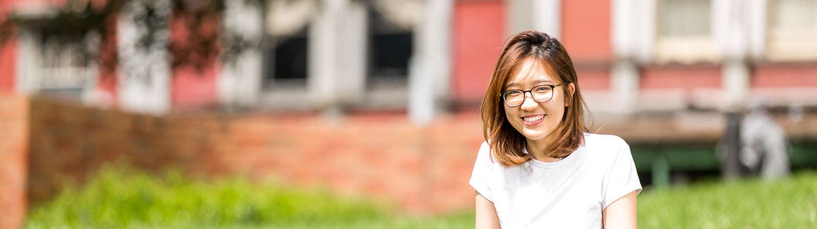 Student smiling sitting on grass outside campus