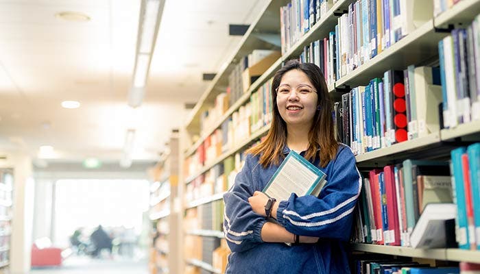 Student smiling and standing by bookshelves in library
