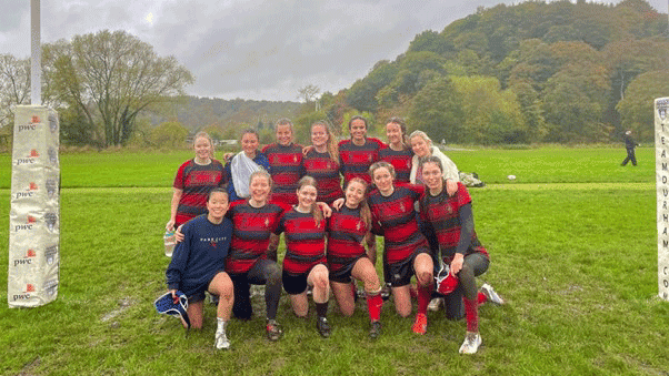 Students in a rugby team in a field smiling at camera