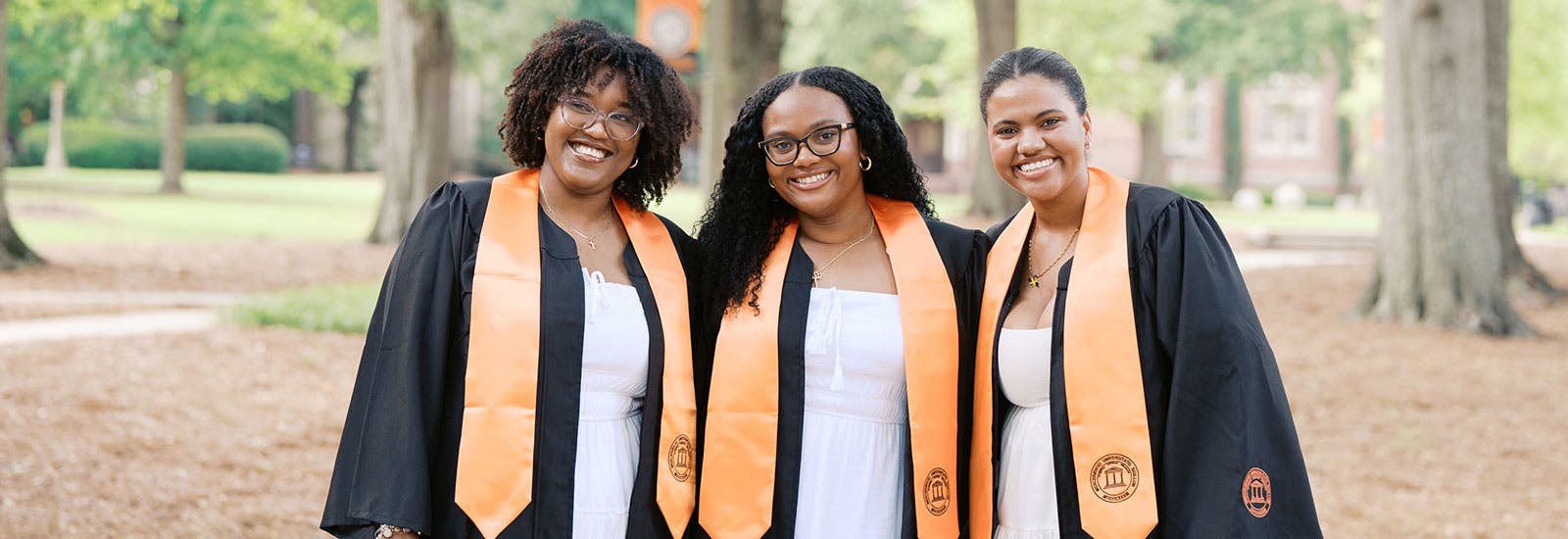 Three graduates smiling outside on campus