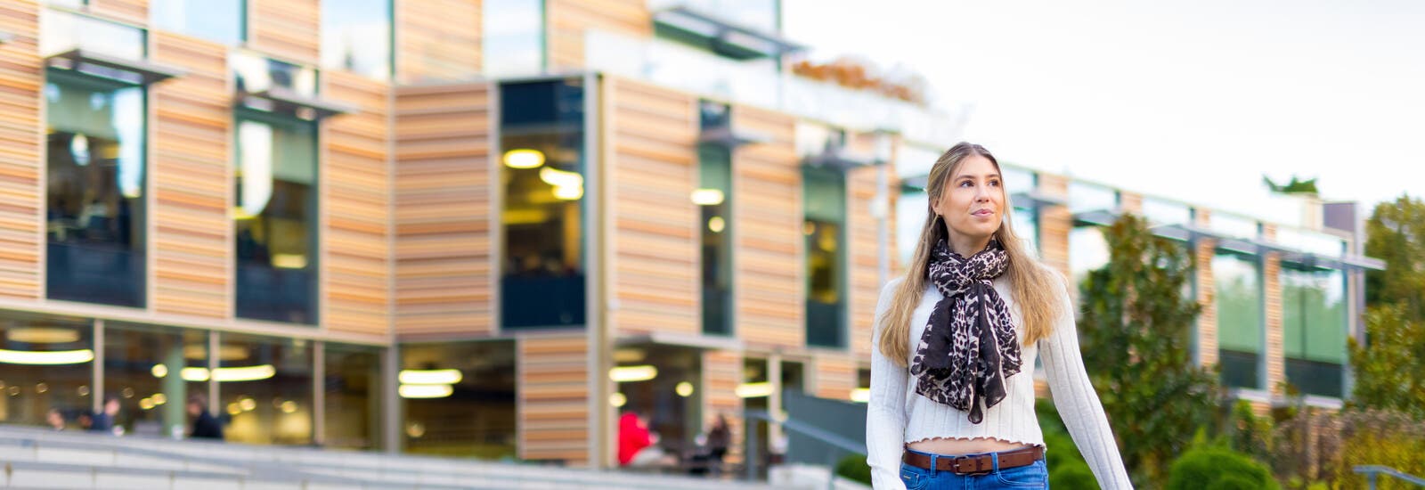 A student walking across RHUL's leafy campus.