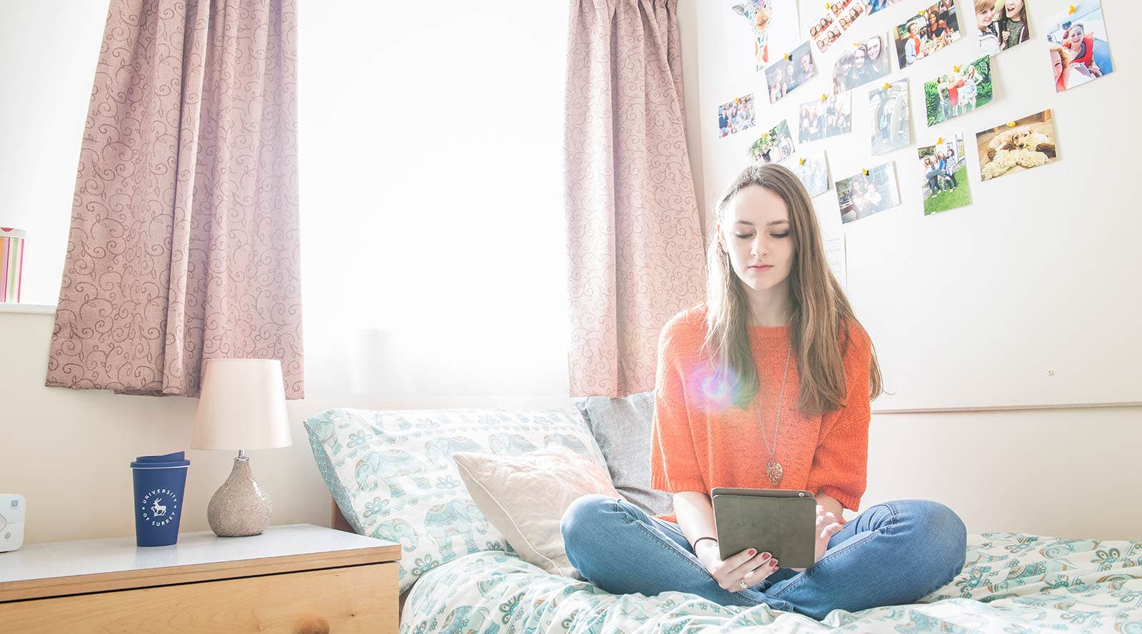 Student sitting on bed in accommodation with tablet