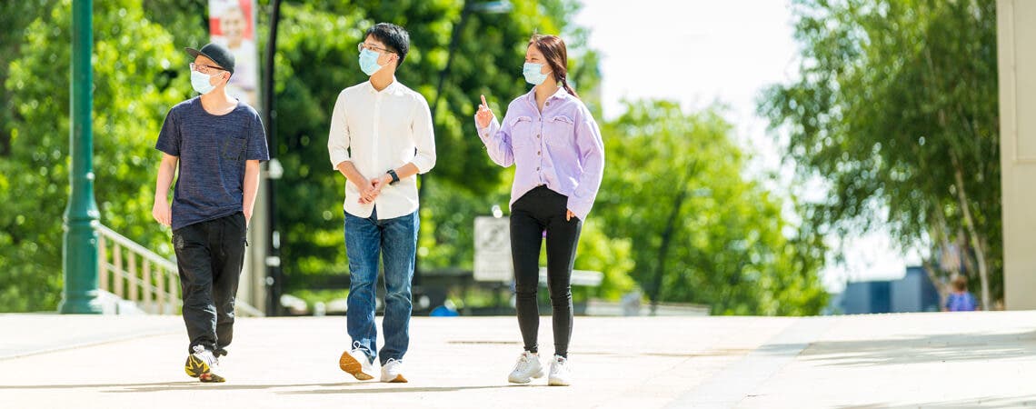 Three students wearing masks walking on campus
