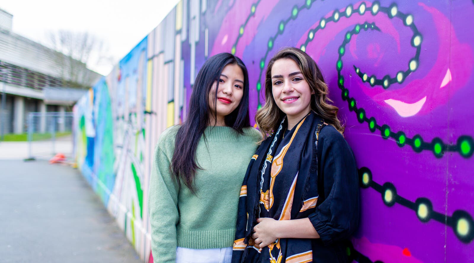 Students smiling and leaning against wall with street art