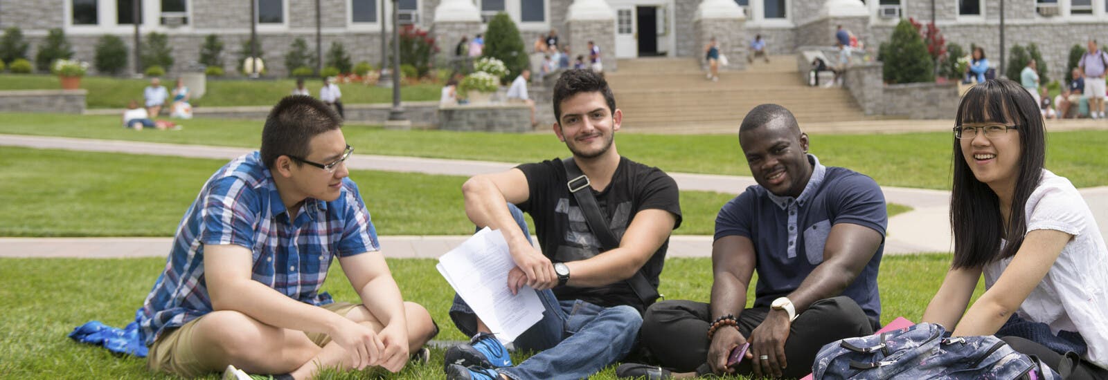 Four students sitting on grass outside campus