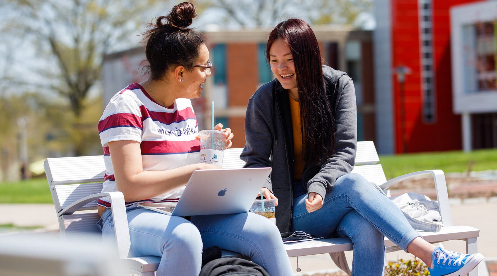 Two students looking at a laptop and drinking coffee outside