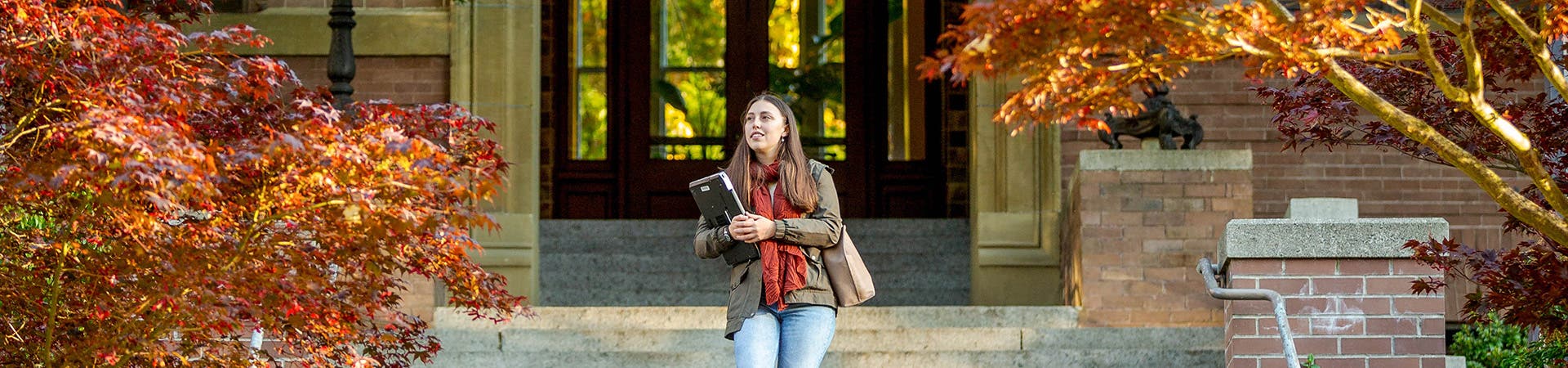 Student walking outside campus holding laptop