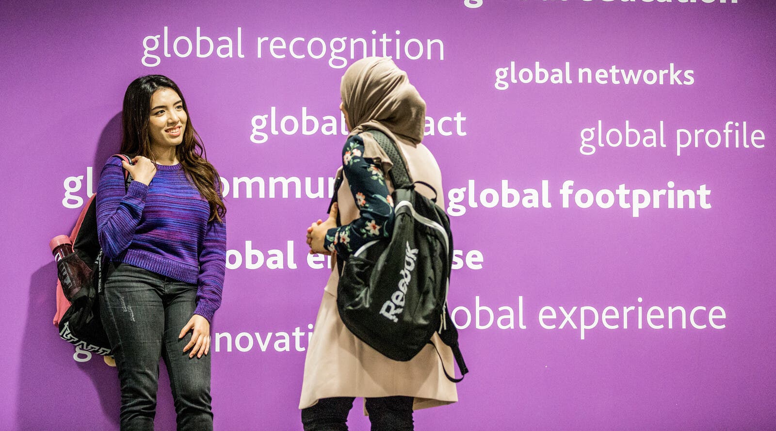 Two international students in front of a bright, purple wall