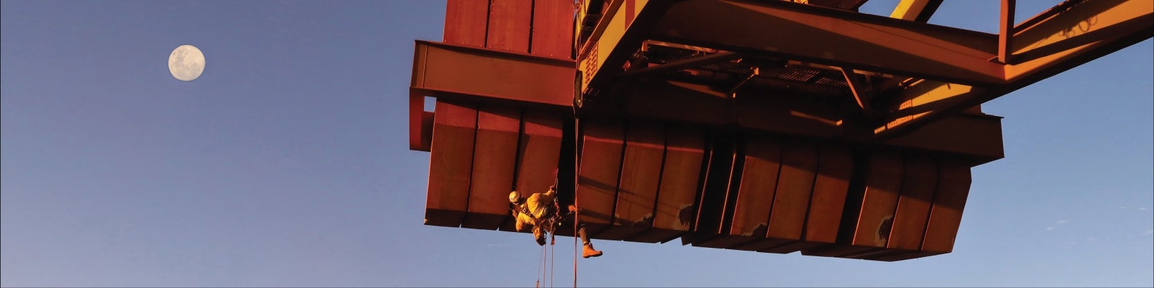 Texcan - Industries (View All) Banner Image: Man with harness climbing large crane in an industrial environment