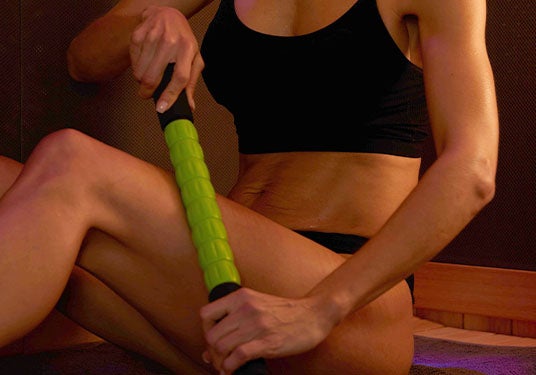 Woman using a massage stick on her legs in the sauna 
