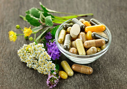 A bowl of vitamin supplements sits on a table next to herbal remedies. 