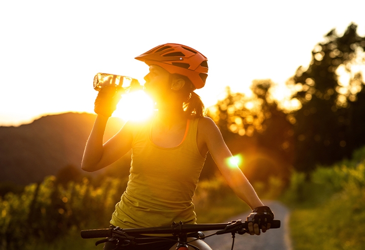 Woman on a bike drinking water at sunset