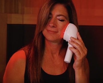 A woman using a LumiNIR wand on her face and smiling
