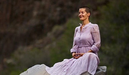 A woman stands peacefully with her eyes closed, enjoying a breeze on a mountain-top 